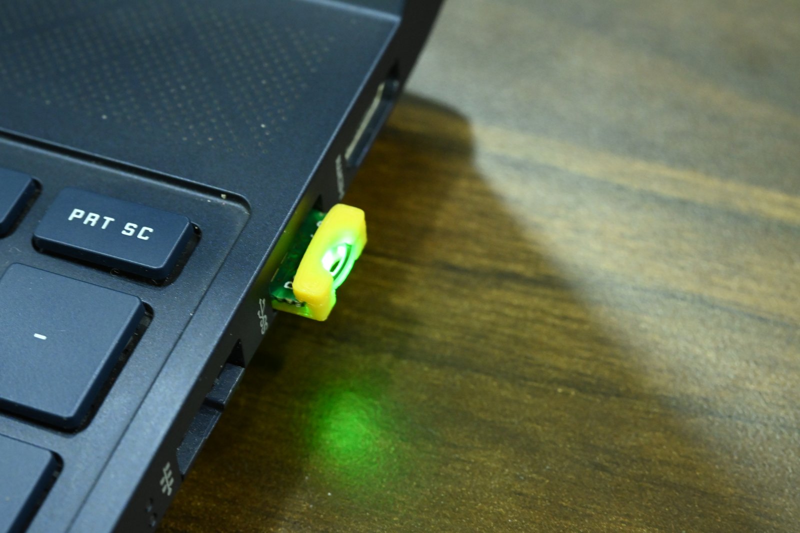 Earlier green Romu prototype with a yellow shim and illuminated LED inserted into a laptop USB Type-A port
