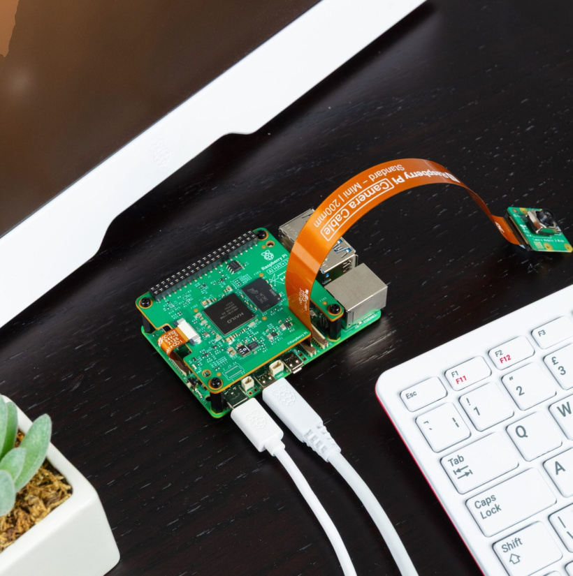 Raspberry Pi 5 with an AI HAT+ 2 and connected camera beside a keyboard on a desk.