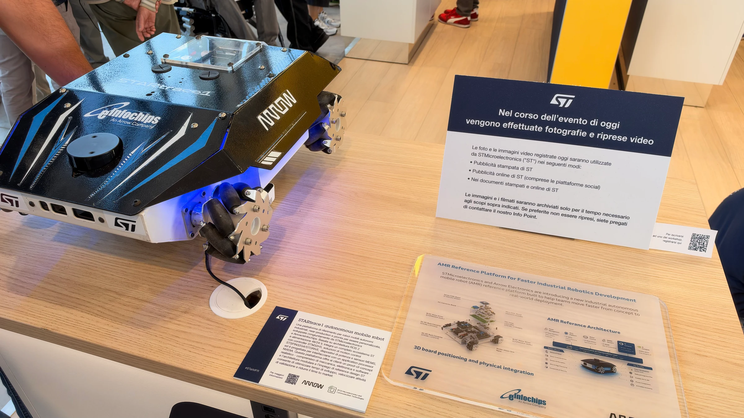 Black-and-blue ST, Arrow, and eInfochips mobile robot with mecanum wheels and a top-mounted lidar scanner beside its architecture diagram.